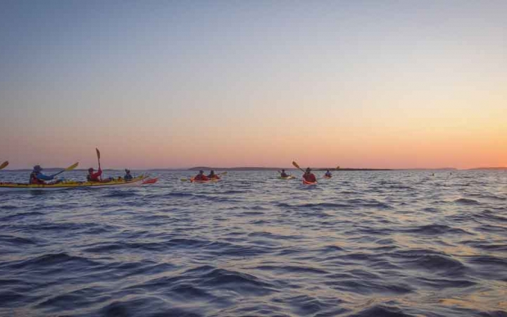 a group of kayaks paddle in open water while the sun sets